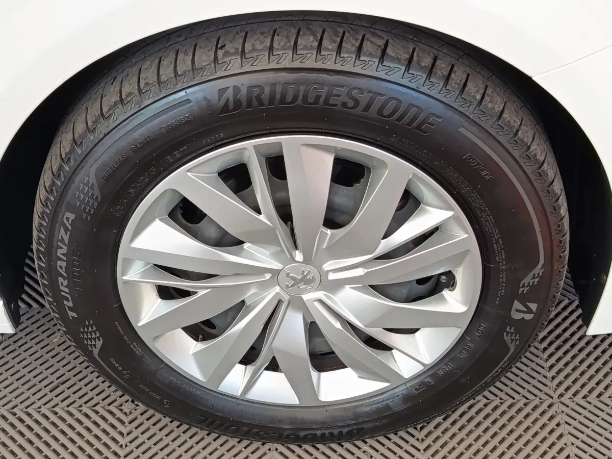Gros plan sur la roue avant droite d'une Peugeot 208 blanche avec jante alliage et pneu Bridgestone Turanza.