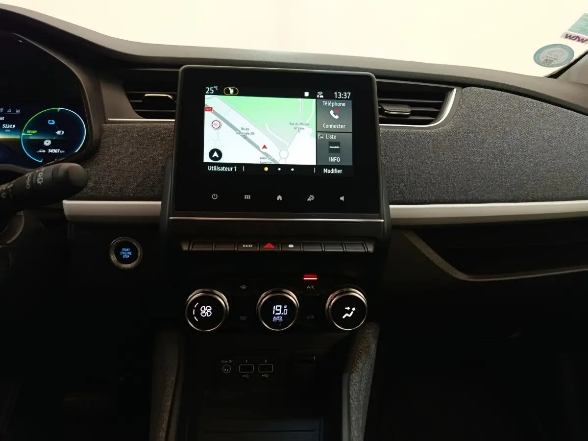 Vue intérieure centrée sur la console centrale de la Renault ZOE blanche 2023 avec écran tactile et commandes climatisation.