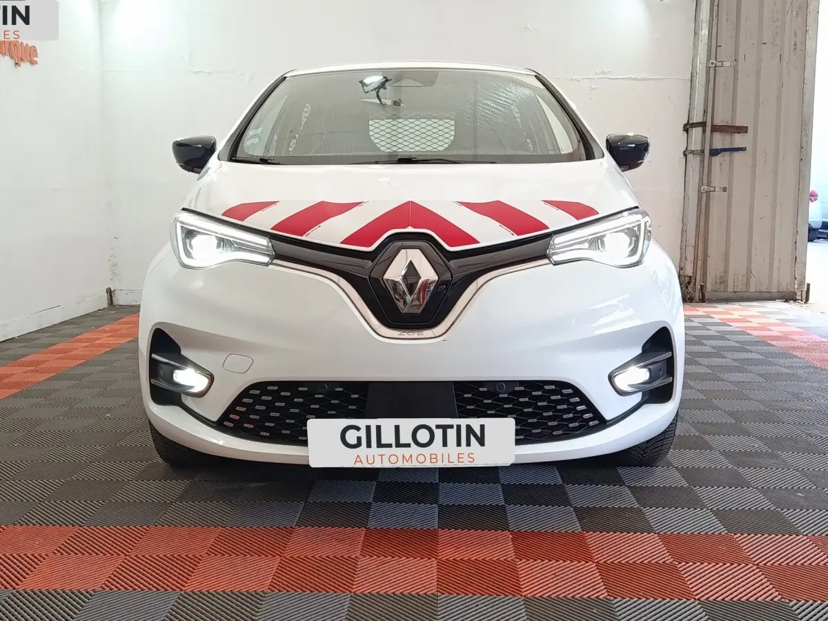 Vue avant d'une Renault ZOE blanche avec bandes rouges diagonales sur le capot et phares LED allumés dans un garage.