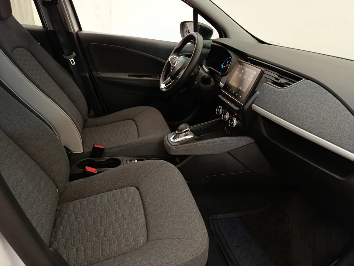 Vue intérieure côté conducteur de la Renault ZOE blanche 2023, avec tableau de bord moderne et sièges gris tissu.