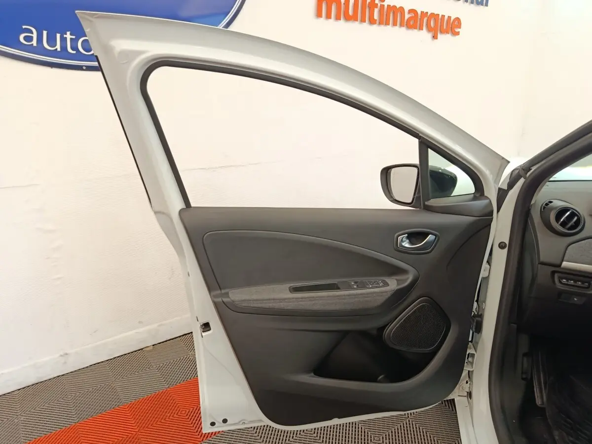 Vue intérieure de la porte avant gauche blanche de la Renault ZOE 2023 avec panneau noir et gris, et commandes électriques.
