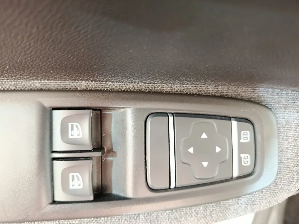 Gros plan sur les commandes électriques des vitres et des rétroviseurs sur la porte côté conducteur d’une Renault ZOE blanche.
