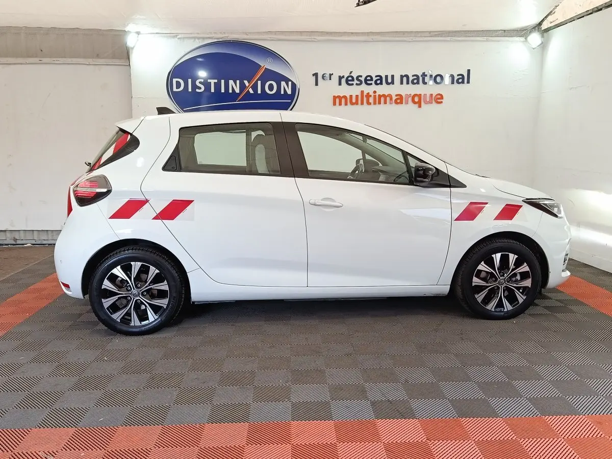 Profil droit de la Renault ZOE blanche 2023 avec bandes rouges sur ailes avant et arrière, jantes noires et grises.