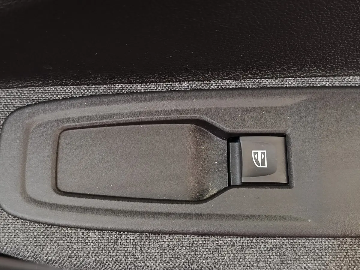 Gros plan sur le bouton de commande électrique de la vitre, intégré dans la garniture intérieure grise de la Renault ZOE blanche.