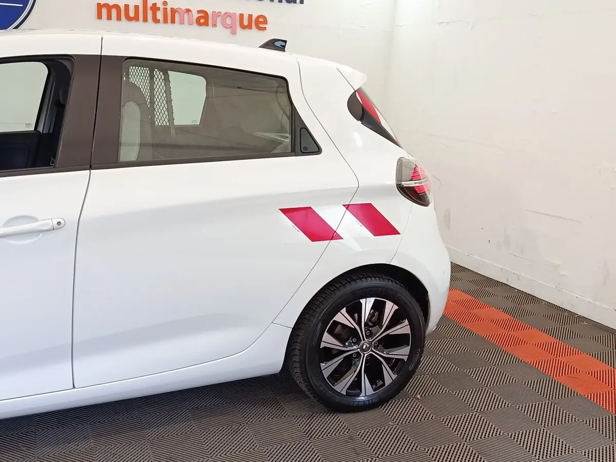 Vue latérale arrière droite d'une Renault ZOE blanche avec marquage rouge sur l'aile arrière et jantes noires.