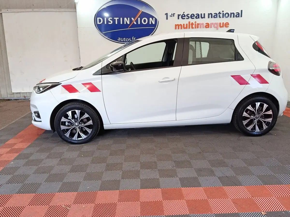 Profil côté gauche de la Renault ZOE blanche 2023 avec marquages rouges et jantes alliage noires et argentées.