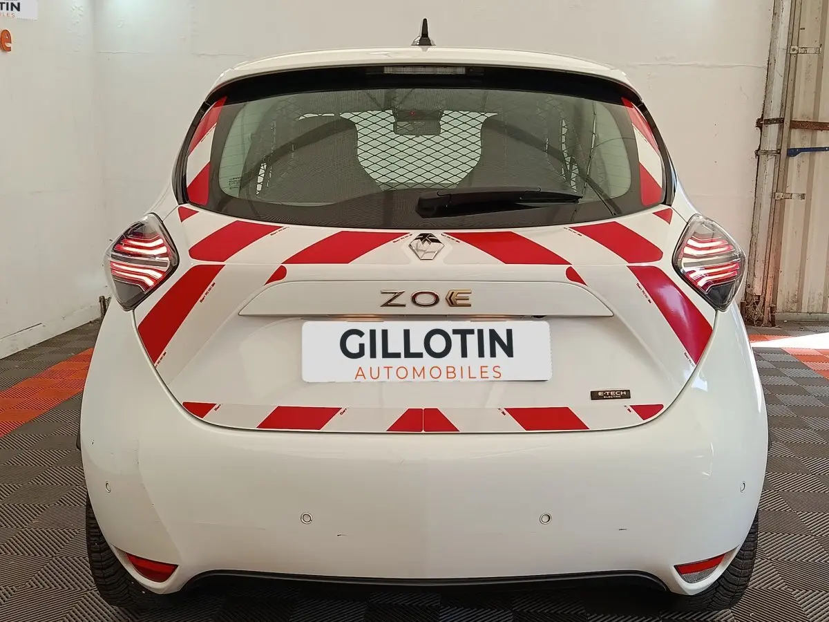 Vue arrière d'une Renault ZOE blanche 2023 avec bandes rouges diagonales de sécurité et feux arrière LED allumés.