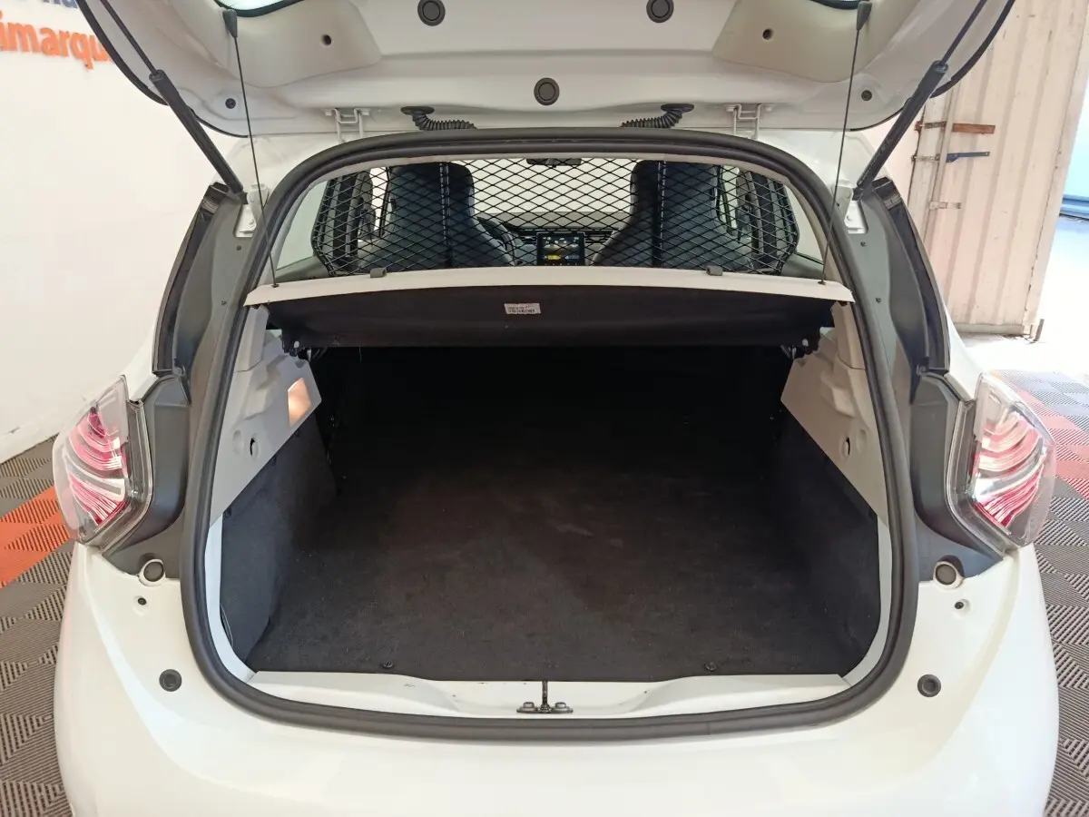Coffre ouvert vu de l'arrière d'une Renault ZOE blanche avec séparation grillagée et banquette avant visible.