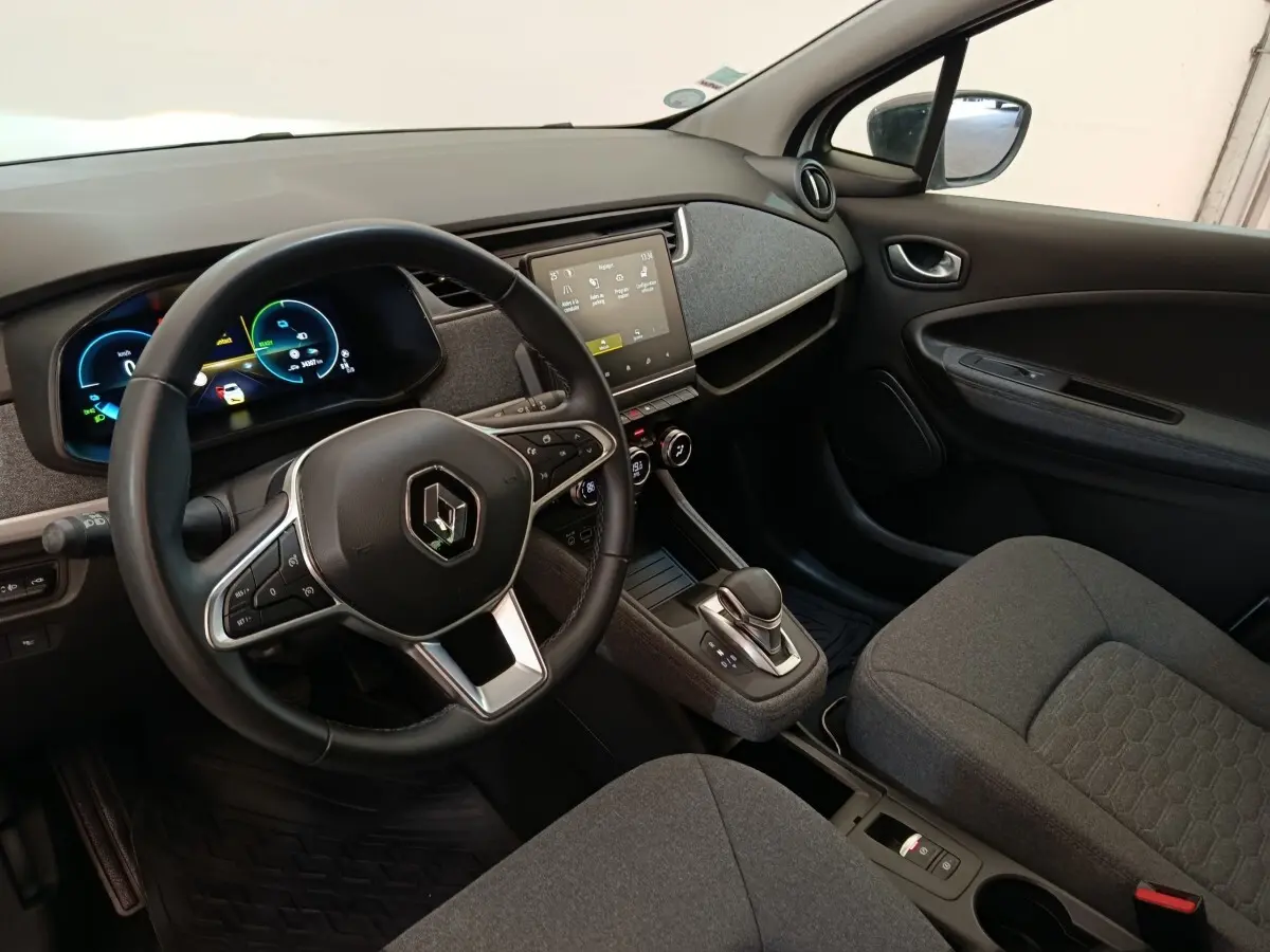 Vue intérieure côté conducteur de la Renault ZOE blanche 2023, volant cuir multifonctions et écran tactile central.