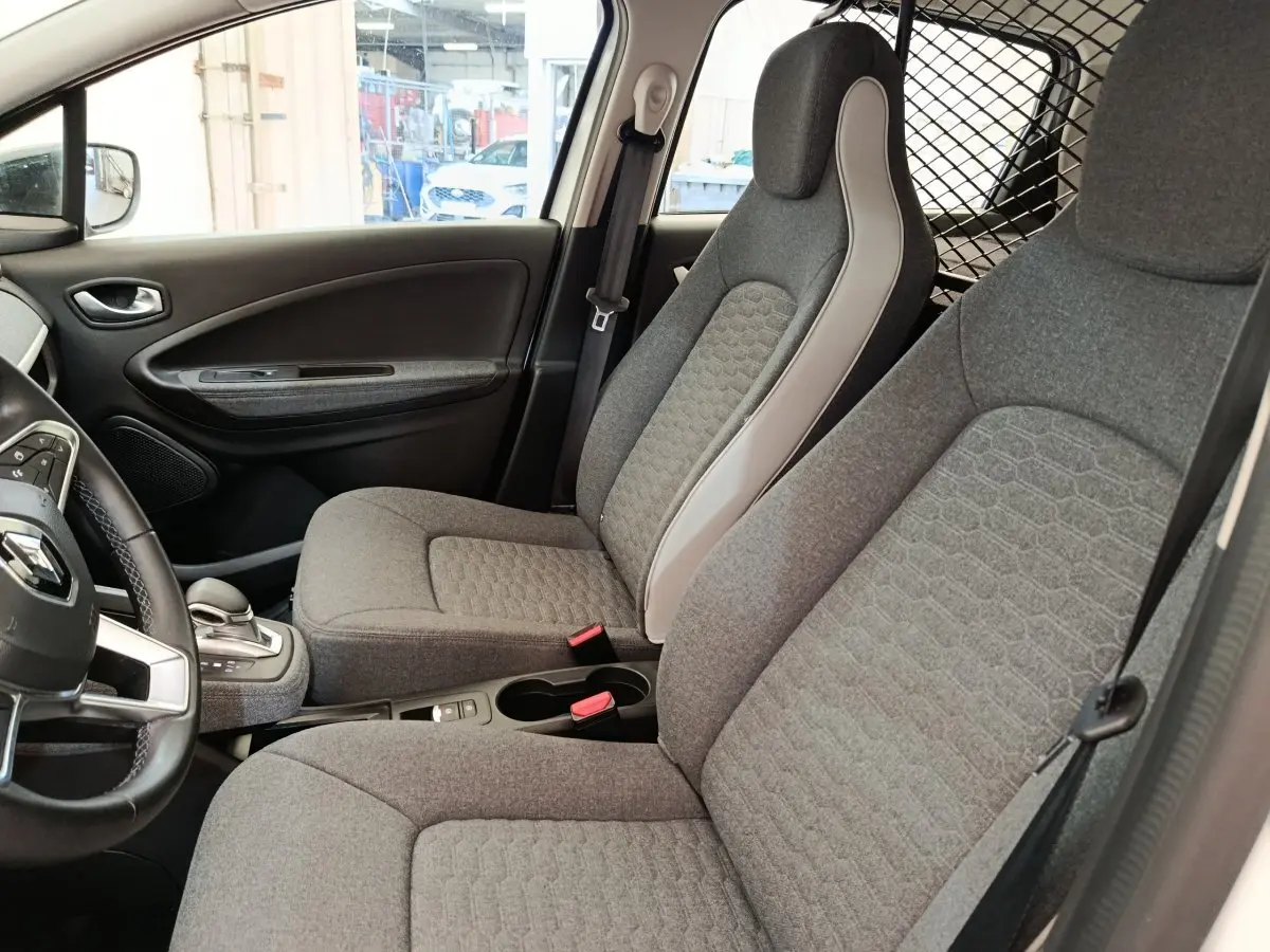 Vue intérieure côté conducteur de la Renault ZOE blanche 2023, sièges gris avec détails clairs et volant multifonctions.