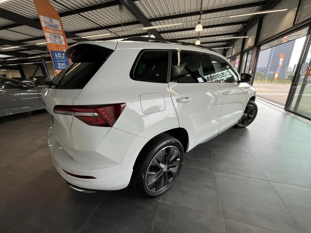 Vue 3/4 arrière droite du SUV blanc SKODA KAROQ 2025 Sportline avec jantes alliage noires et vitres teintées.