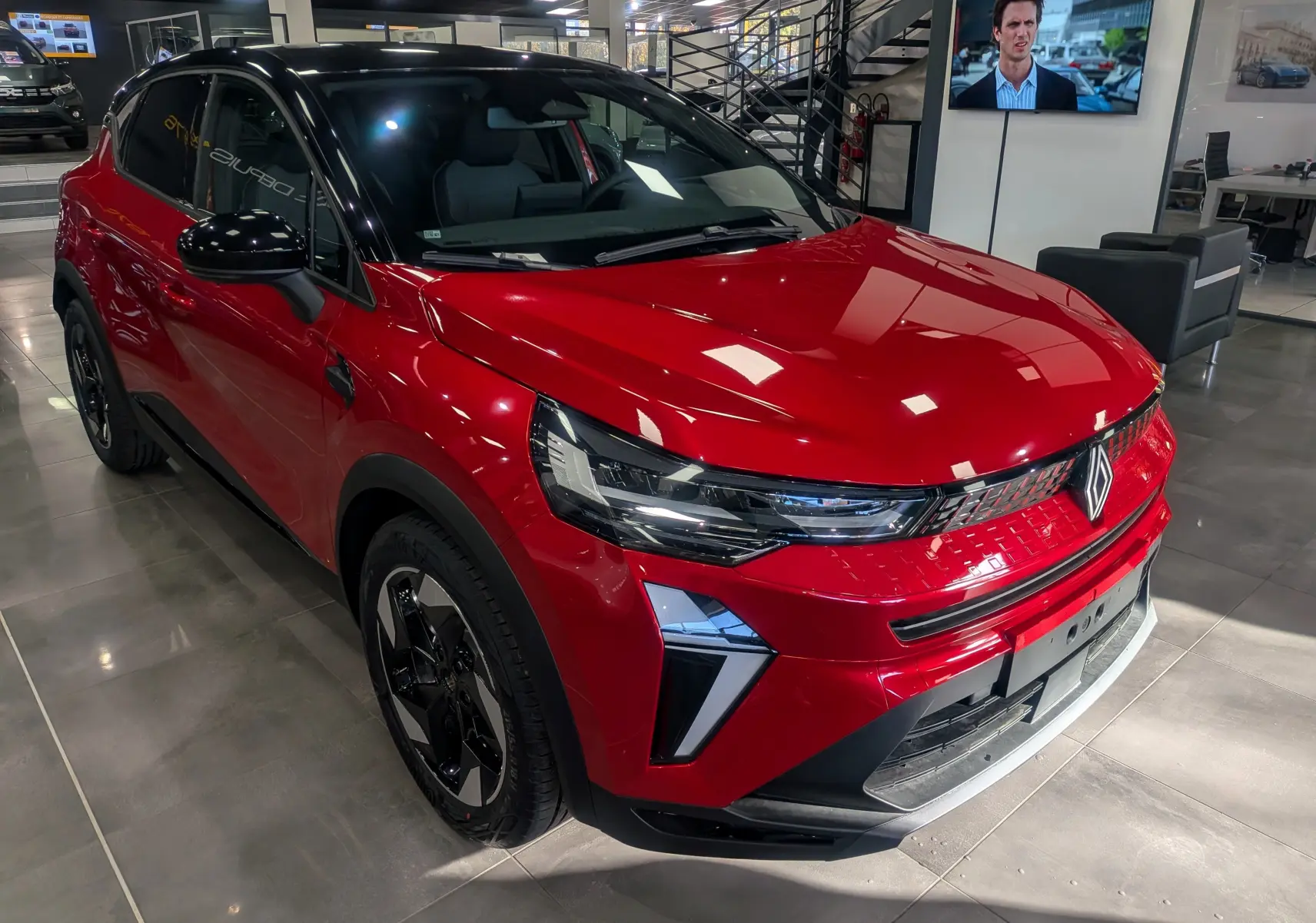 Vue 3/4 avant gauche du Renault Captur E-TECH rouge Flamme avec toit noir et jantes noires en showroom.