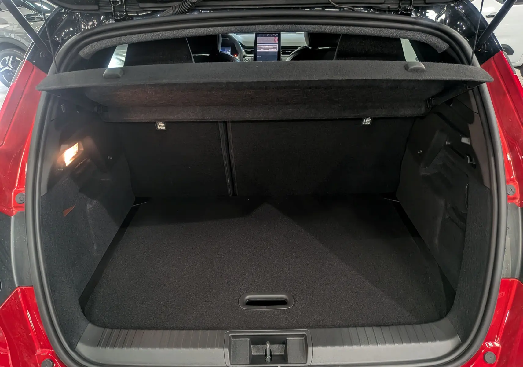 Coffre ouvert vu de l'arrière d'un Renault Captur E-Tech rouge flamme avec toit noir, intérieur noir et tablette de coffre relevée.