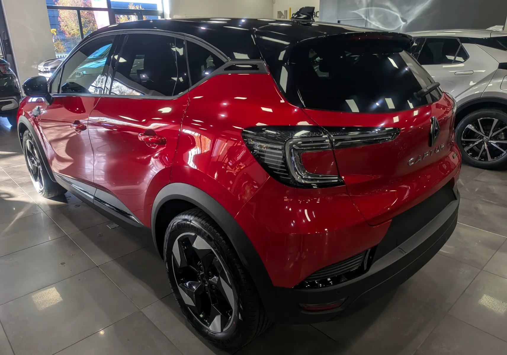 Renault Captur E-TECH hybride rouge Flamme avec toit noir, vue 3/4 arrière droit en showroom lumineux.