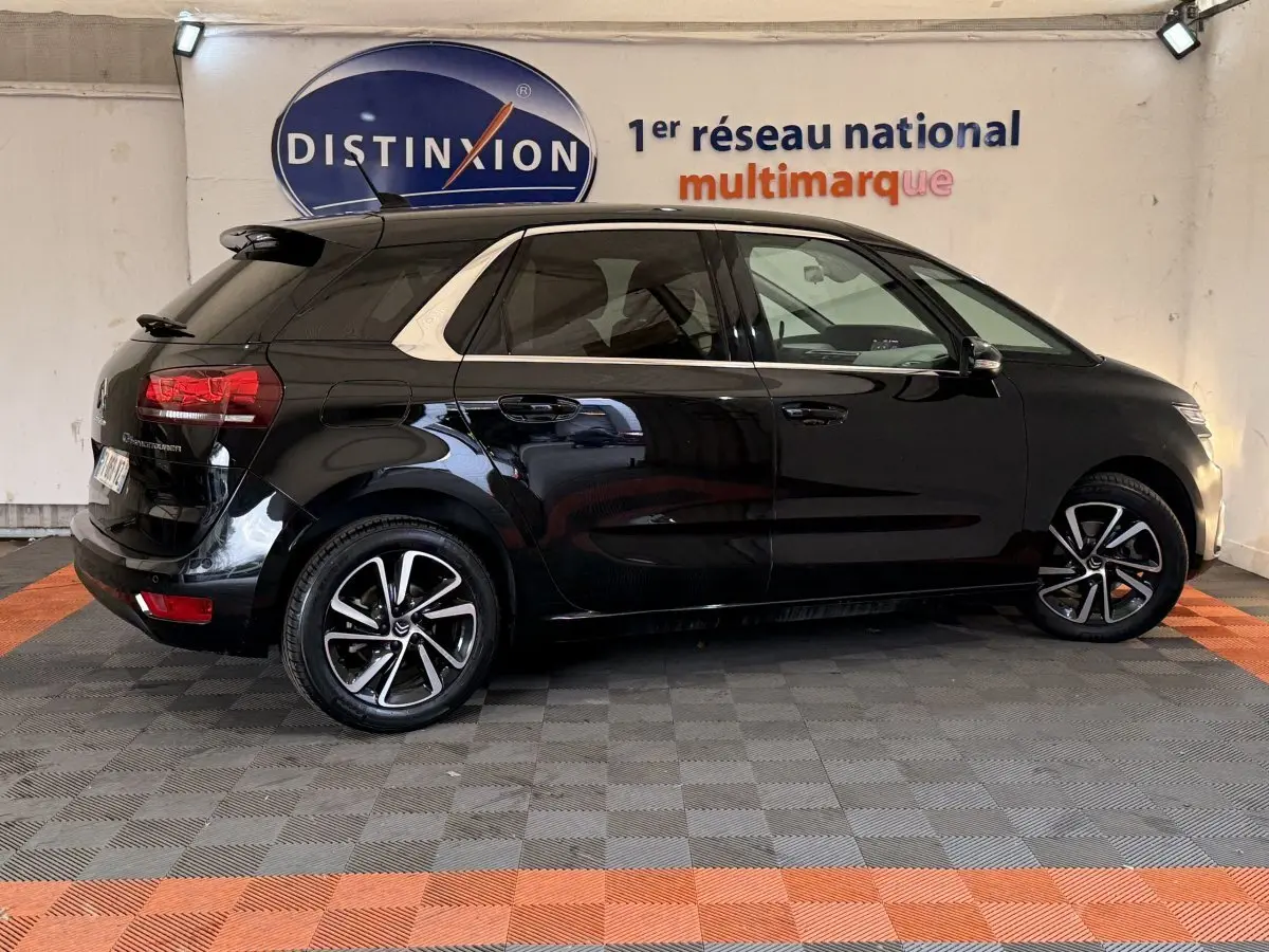 Vue latérale droite d'une Citroën C4 Spacetourer noire avec jantes alliage et toit noir brillant en intérieur showroom.