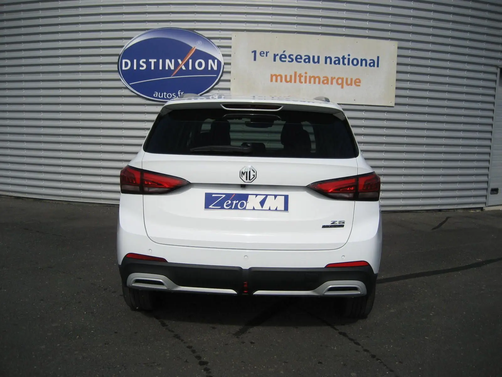 Vue arrière d’un MG ZS blanc 2026 avec feux rouges, logo MG central et plaque « Zero KM » visible.