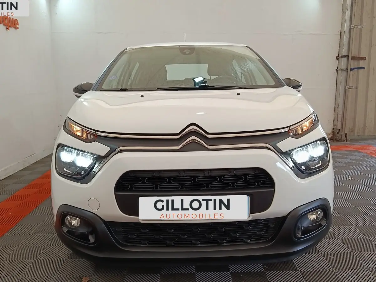 Vue frontale d'une Citroën C3 blanche 2022 avec phares LED allumés dans un garage.