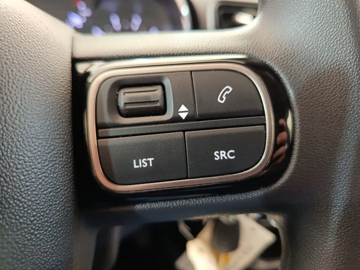 Gros plan sur les commandes au volant noir de la Citroën C3 PureTech 2022, boutons LIST, SRC et téléphone.