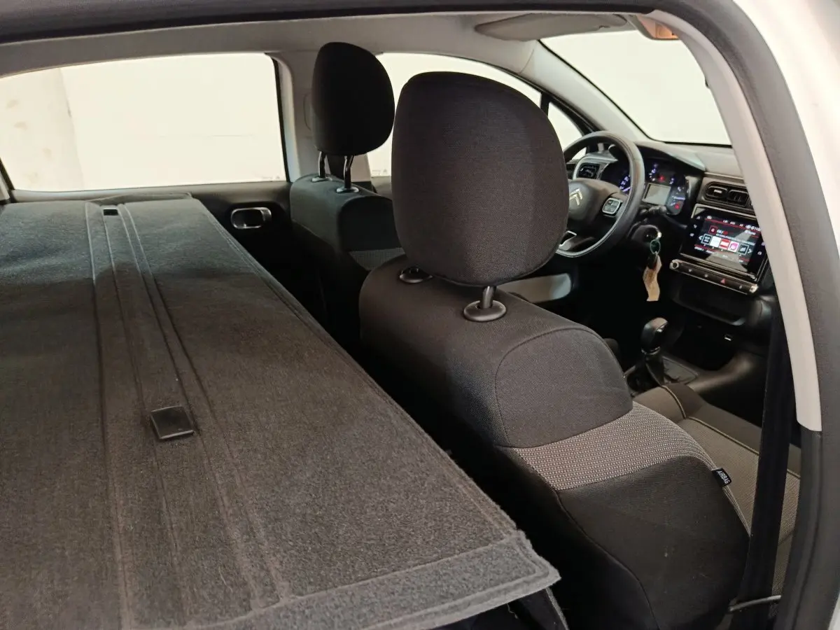 Vue intérieure arrière droite de la Citroën C3 blanche, sièges rabattus et tableau de bord avec écran tactile visible.