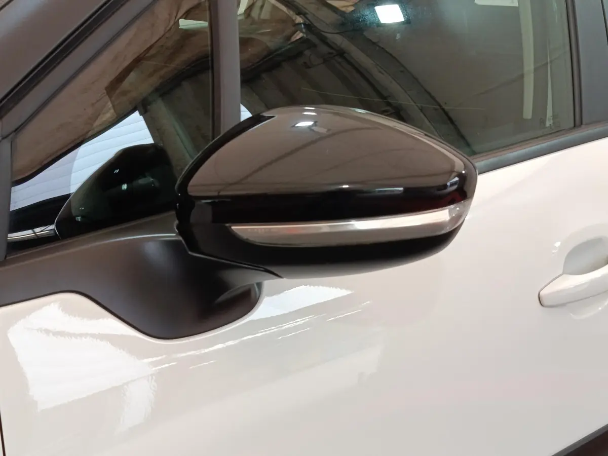 Rétroviseur noir avec clignotant intégré sur porte blanche d'une Citroën C3 PureTech vue de près côté gauche.