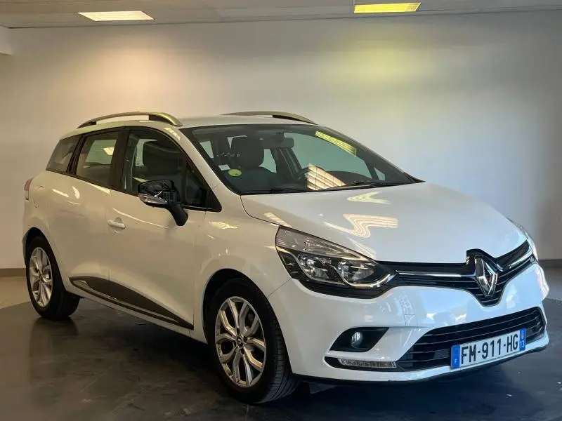 Renault Clio Estate blanc glacier vue 3/4 avant droit avec barres de toit et jantes alliage.