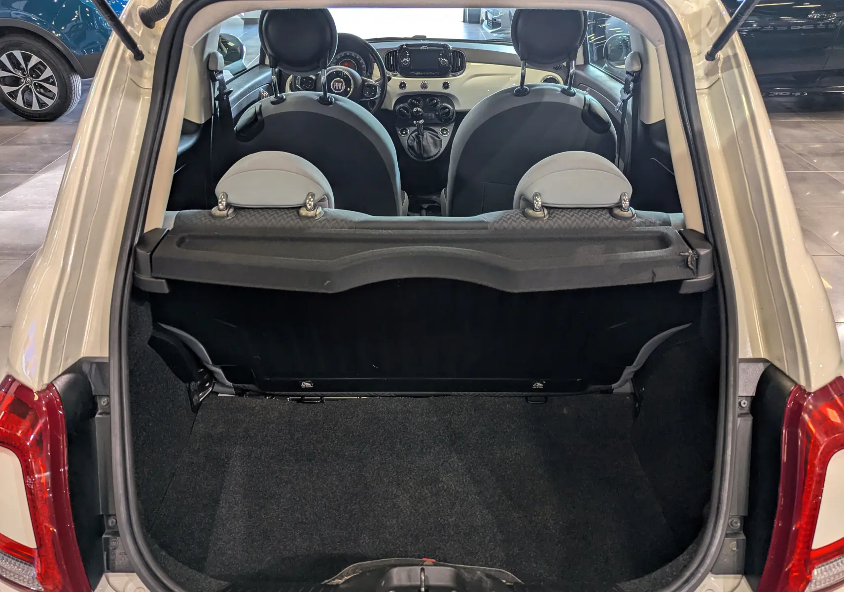Coffre ouvert d'une FIAT 500 Blanc Bossanova vue de l'arrière, avec intérieur noir et tableau de bord visible.