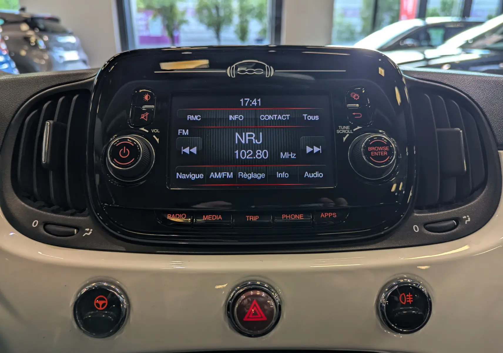 Gros plan sur la console centrale noire et blanche du Fiat 500 Blanc Bossanova avec écran radio affichant NRJ 102.80 MHz.