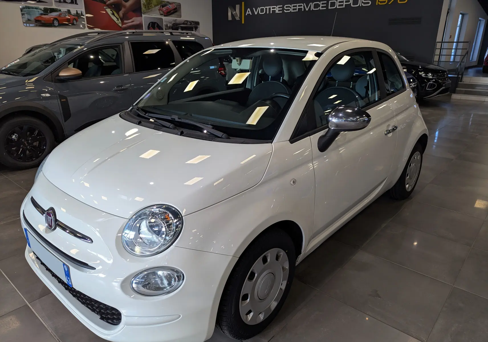 Fiat 500 blanc Bossanova vue 3/4 avant droit en showroom, avec rétroviseurs chromés et jantes acier.