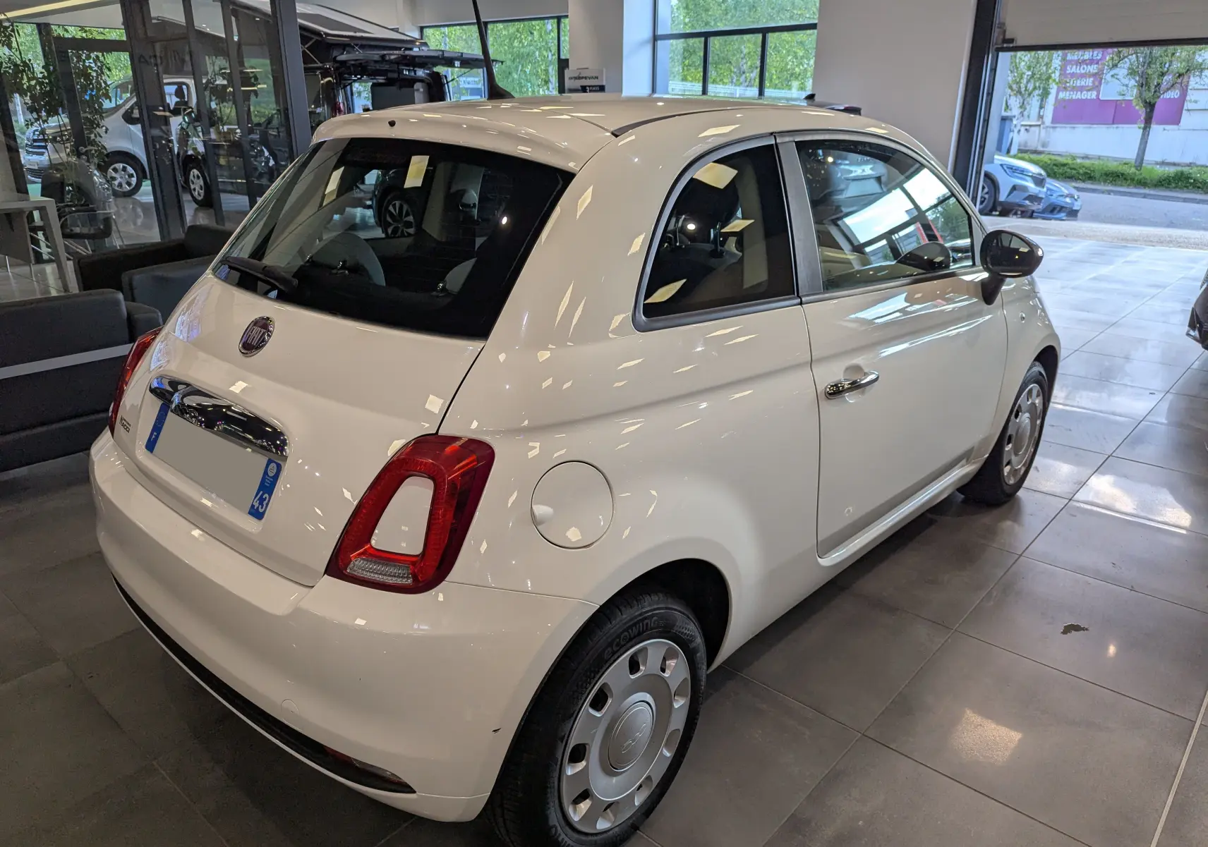 Vue 3/4 arrière droite d'une FIAT 500 blanche Bossanova dans un showroom, avec jantes acier et rétroviseurs noirs.