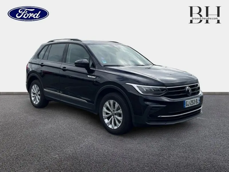 Volkswagen Tiguan noir intense nacré vu en 3/4 avant droit, avec jantes alu et barres de toit visibles.