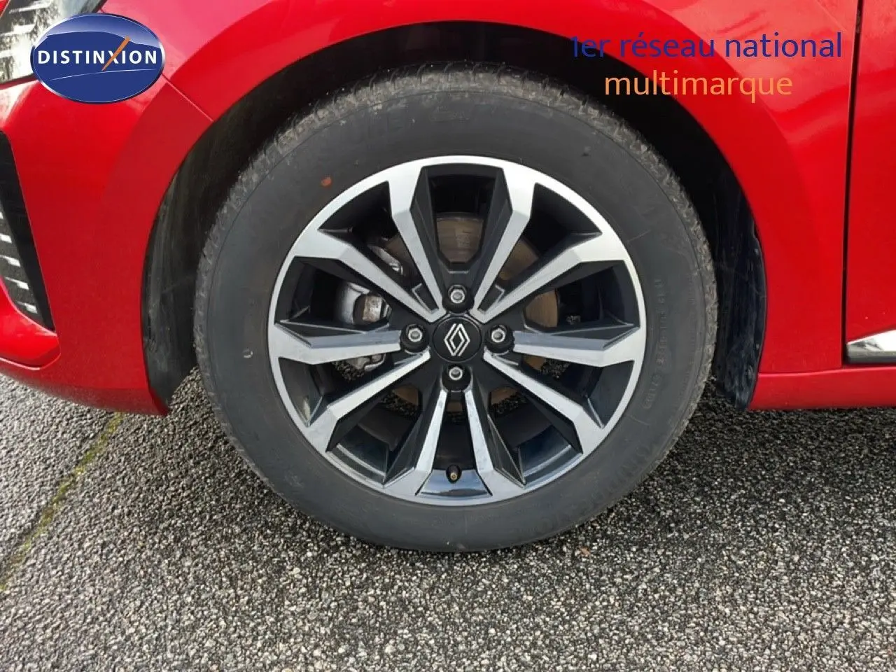 Gros plan sur la roue avant droite d'une Renault Clio rouge Désir Métal avec jante alliage au design moderne.