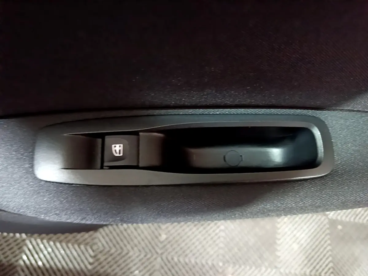 Gros plan sur le bouton de commande de lève-vitre noir dans l'accoudoir intérieur d'une Renault Mégane Business Blue dCi 115 EDC gris clair.