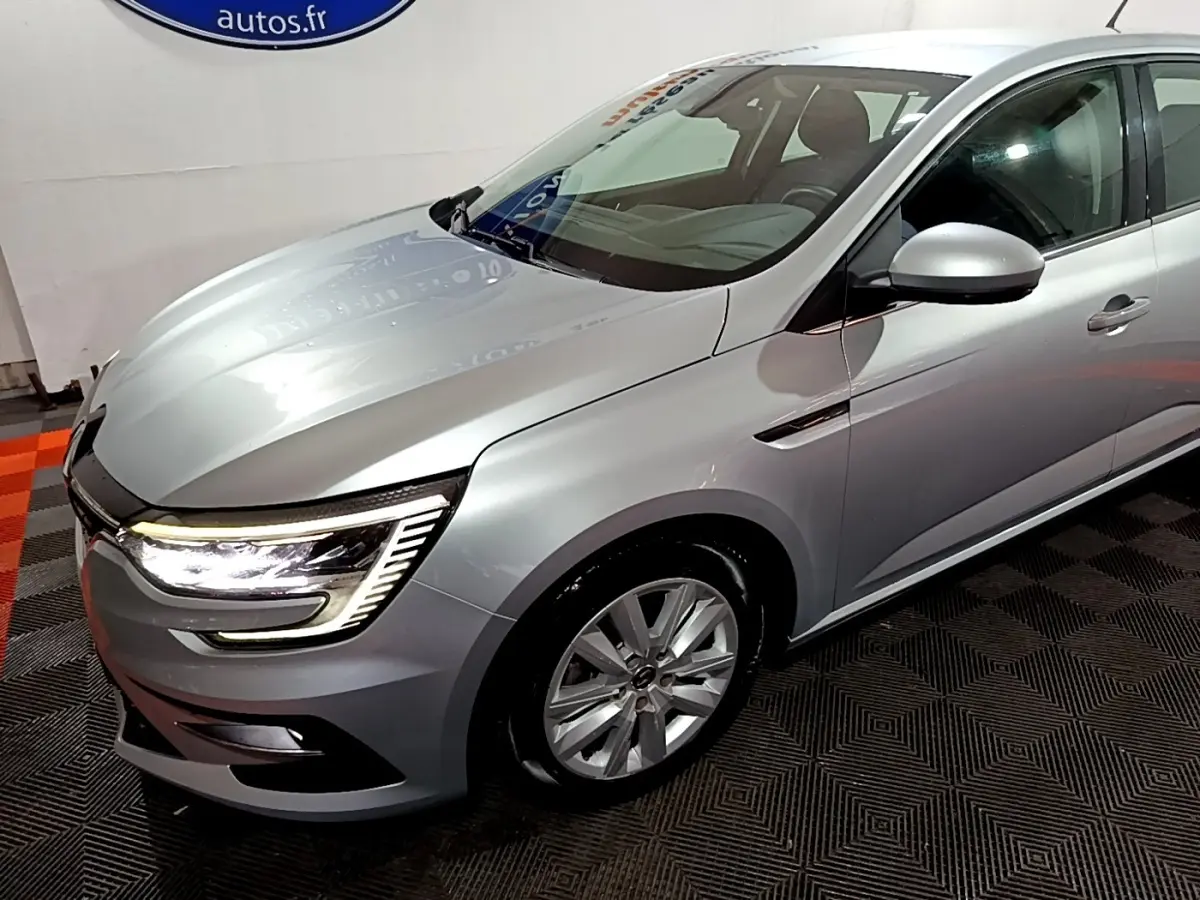 Vue 3/4 avant droit d'une Renault Mégane Business Blue dCi 115 EDC gris clair avec feux LED allumés.