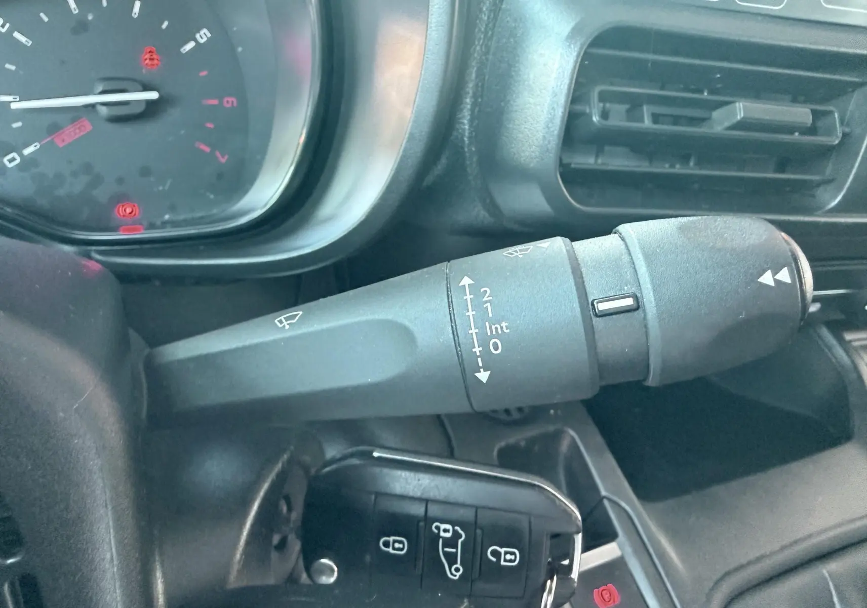 Gros plan sur la commande d’essuie-glace et le tableau de bord intérieur du Citroën Berlingo 2019 blanc.