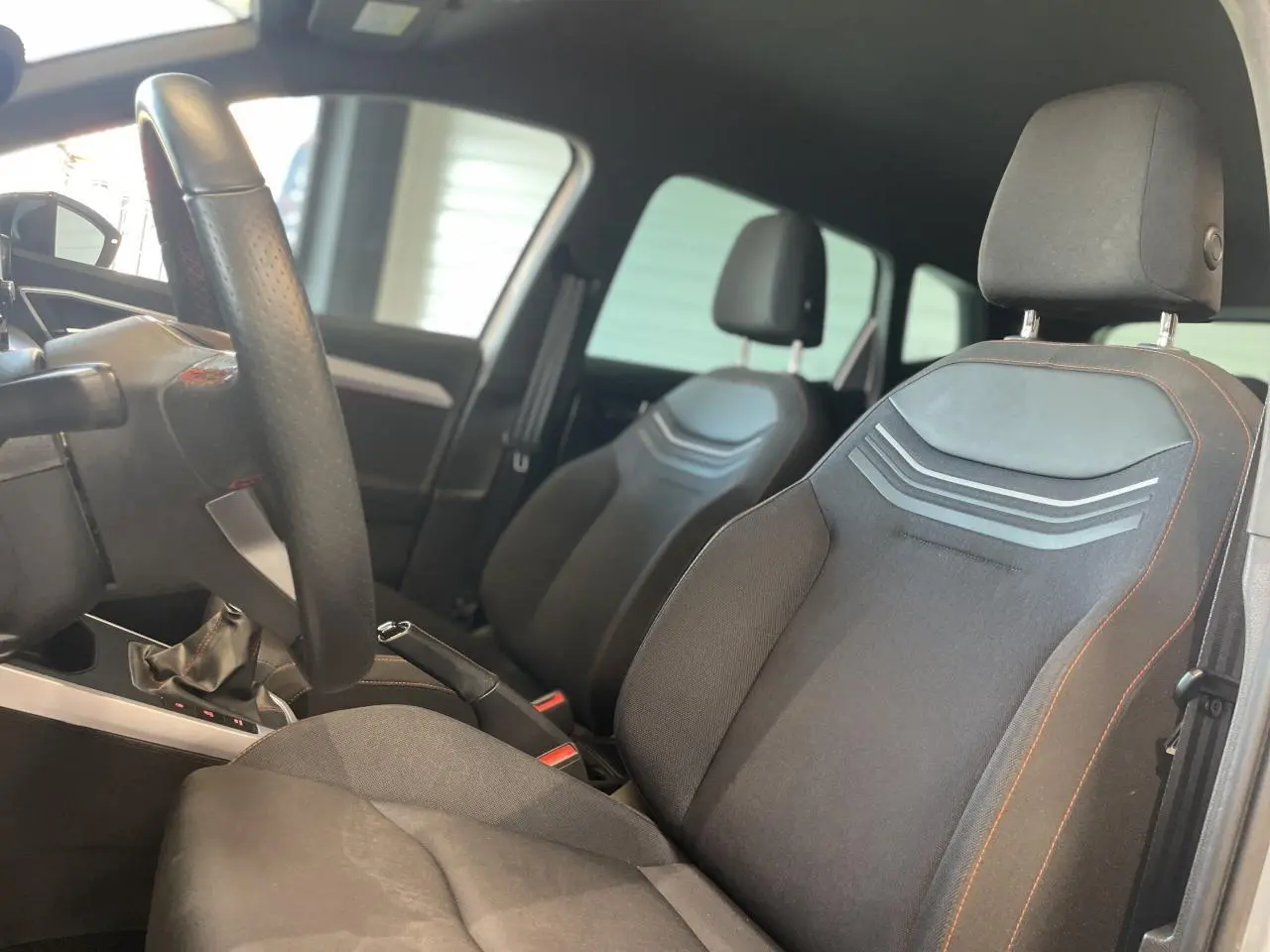 Intérieur avant du SEAT Arona 2024, sièges textile noirs avec surpiqûres orange et volant sport cuir à méplat.