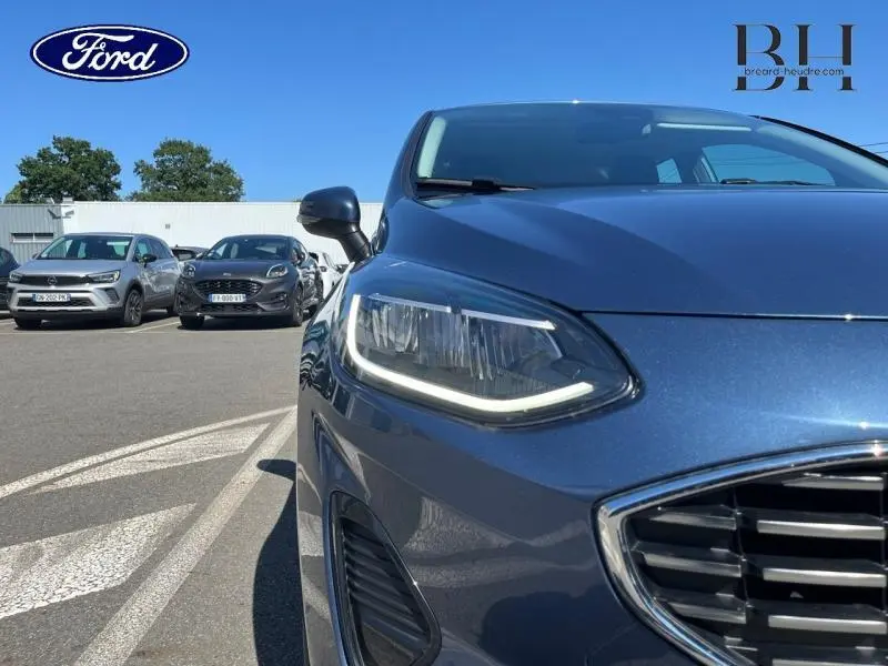 Gros plan sur l'avant droit d'une Ford Fiesta 2022 bleu azur métallisé avec phares LED et calandre chromée.