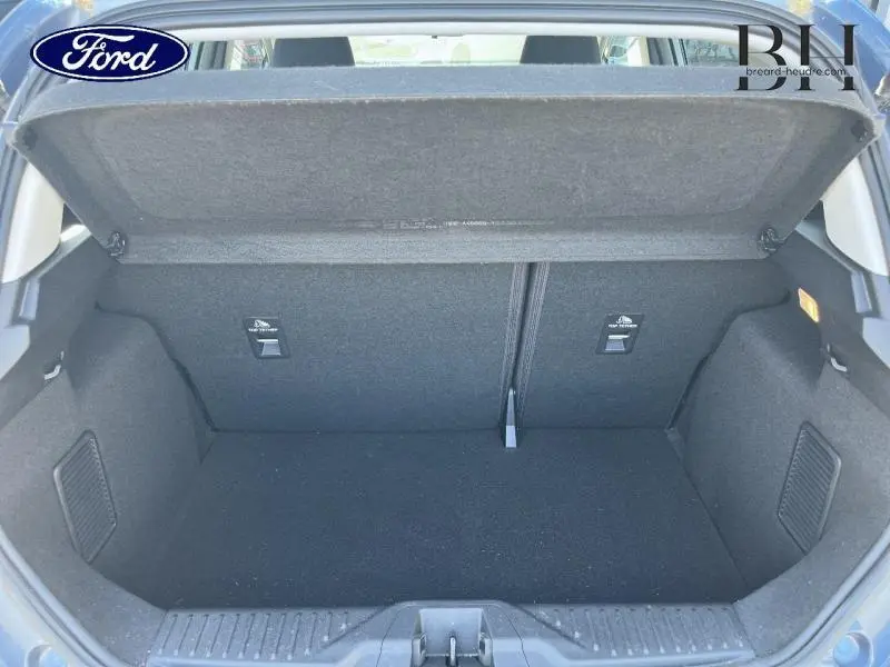 Coffre ouvert vu de l'arrière d'une Ford Fiesta 2022 bleu azur métallisée, intérieur noir et espace de rangement visible.