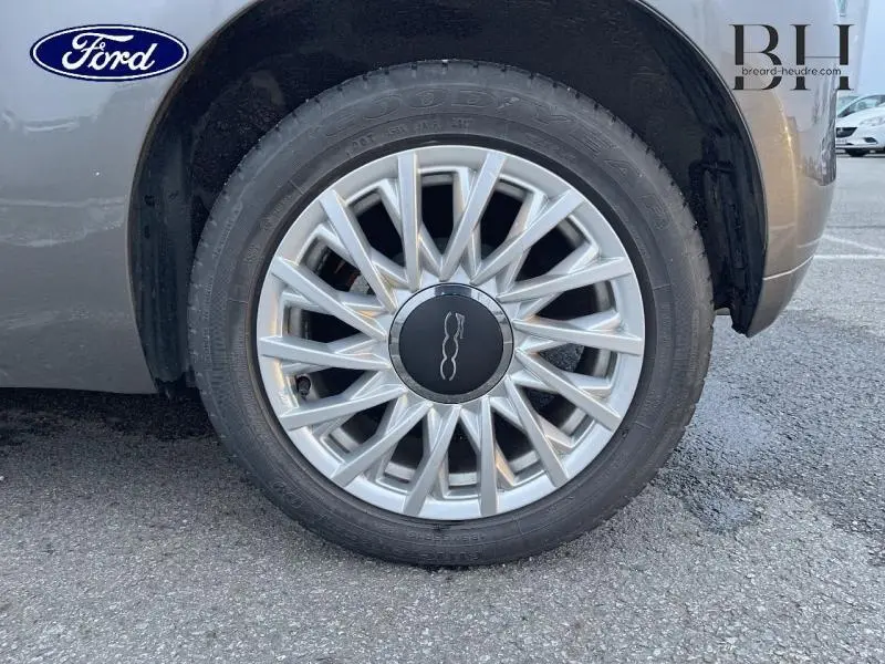 Gros plan sur la roue avant droite d'une FIAT 500 gris métal avec jante alliage au design étoilé.