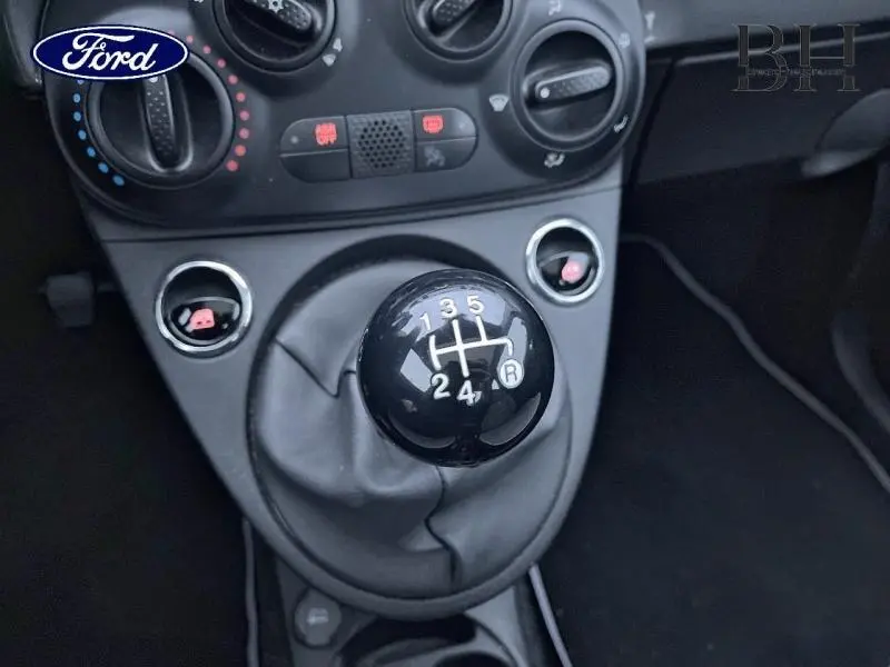 Gros plan sur le levier de vitesses manuel noir et le tableau de bord gris foncé d'une Fiat 500 Lounge 2018.