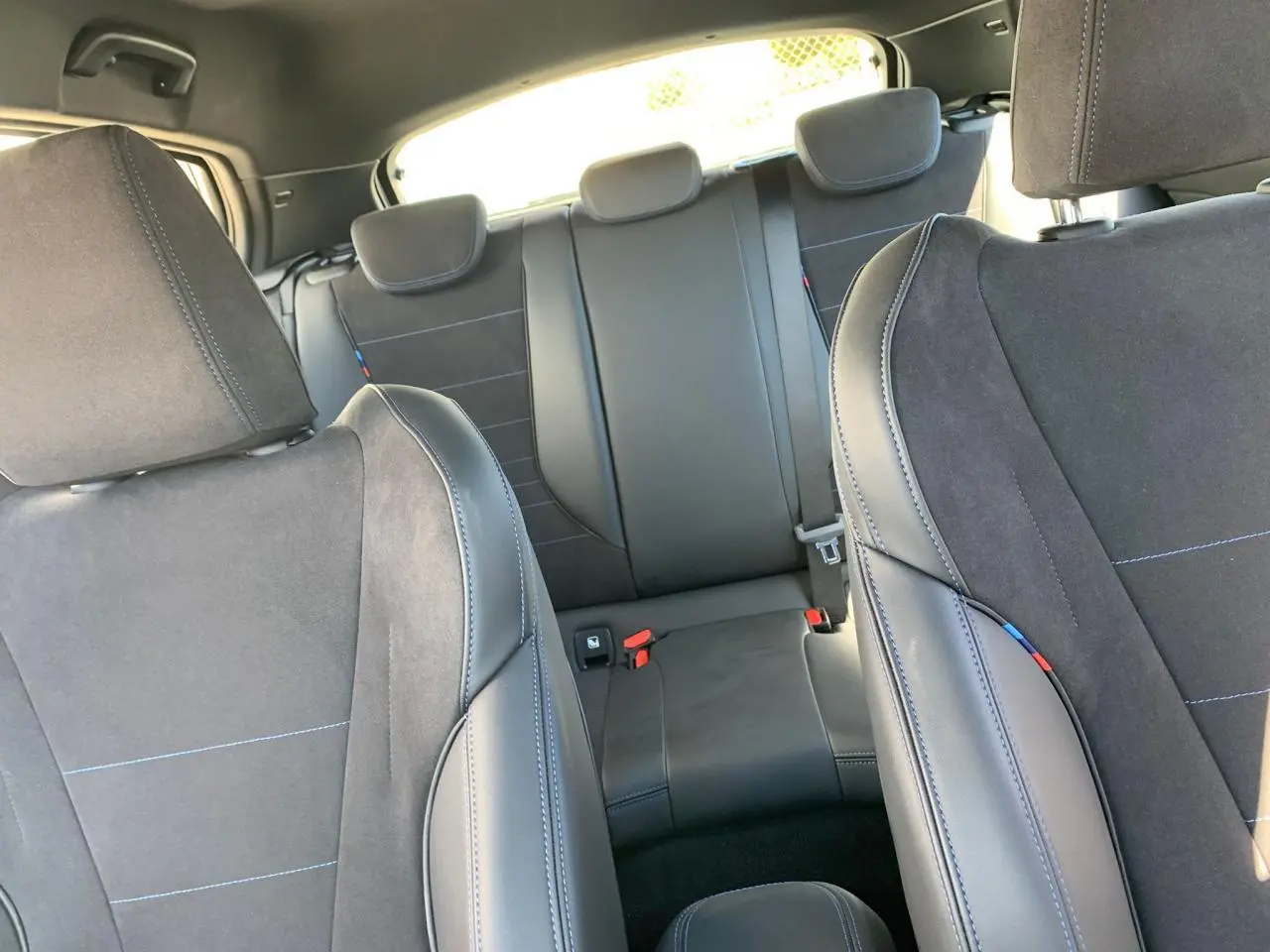 Vue intérieure des sièges avant et arrière en Alcantara noir avec surpiqûres bleues d'une BMW Série 1 118d M Sport.
