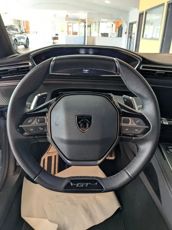 Volant cuir noir avec logo Peugeot et inscription GT au centre du tableau de bord d'une 508 SW gris selenium 2024.