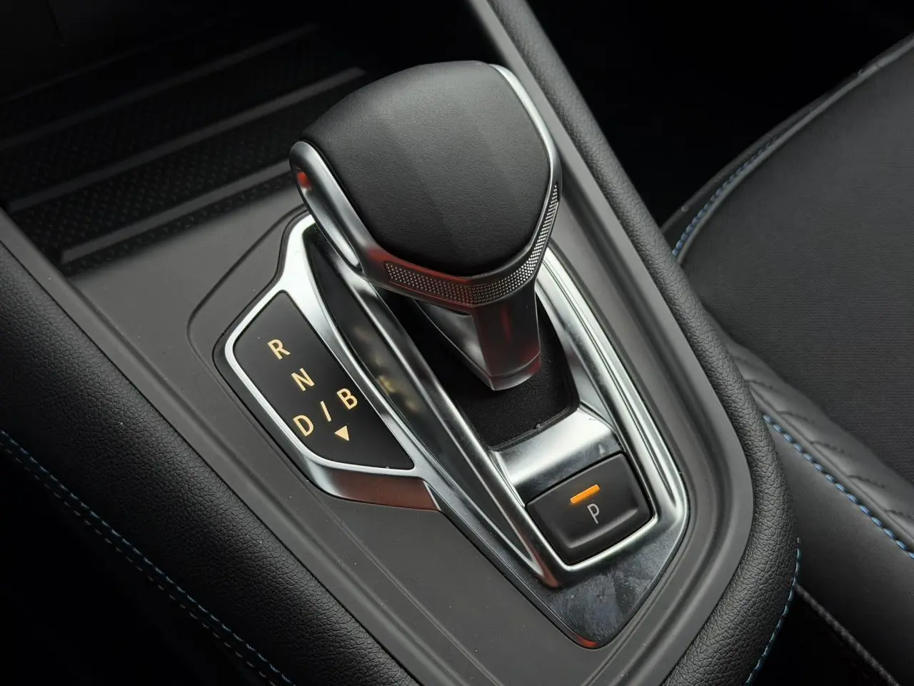 Gros plan sur la commande de boîte automatique du Renault Captur Bleu Iron, avec surpiqûres bleues visibles sur l'accoudoir.