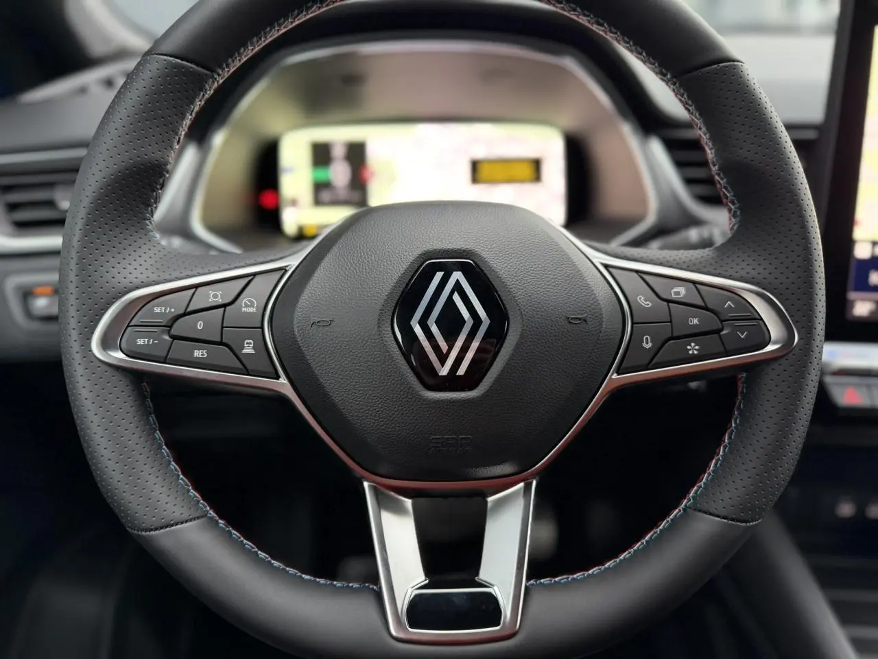 Gros plan sur le volant noir perforé avec surpiqûres bleu blanc rouge du Renault Captur Bleu Iron, tableau de bord numérique flou en arrière-plan.