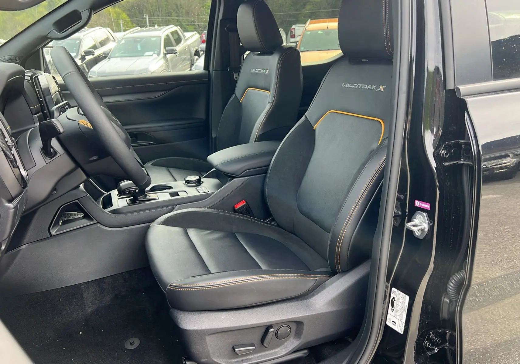 Vue intérieure côté conducteur du Ford Ranger 205 Wildtrak X noir agate, sièges en cuir avec surpiqûres orange et logo Wildtrak X brodé.