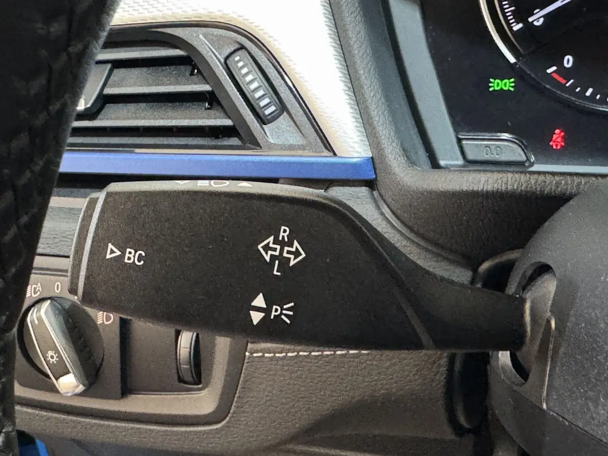 Gros plan sur la manette de clignotant gauche du BMW X2 bleu, avec tableau de bord et aérateur visibles.