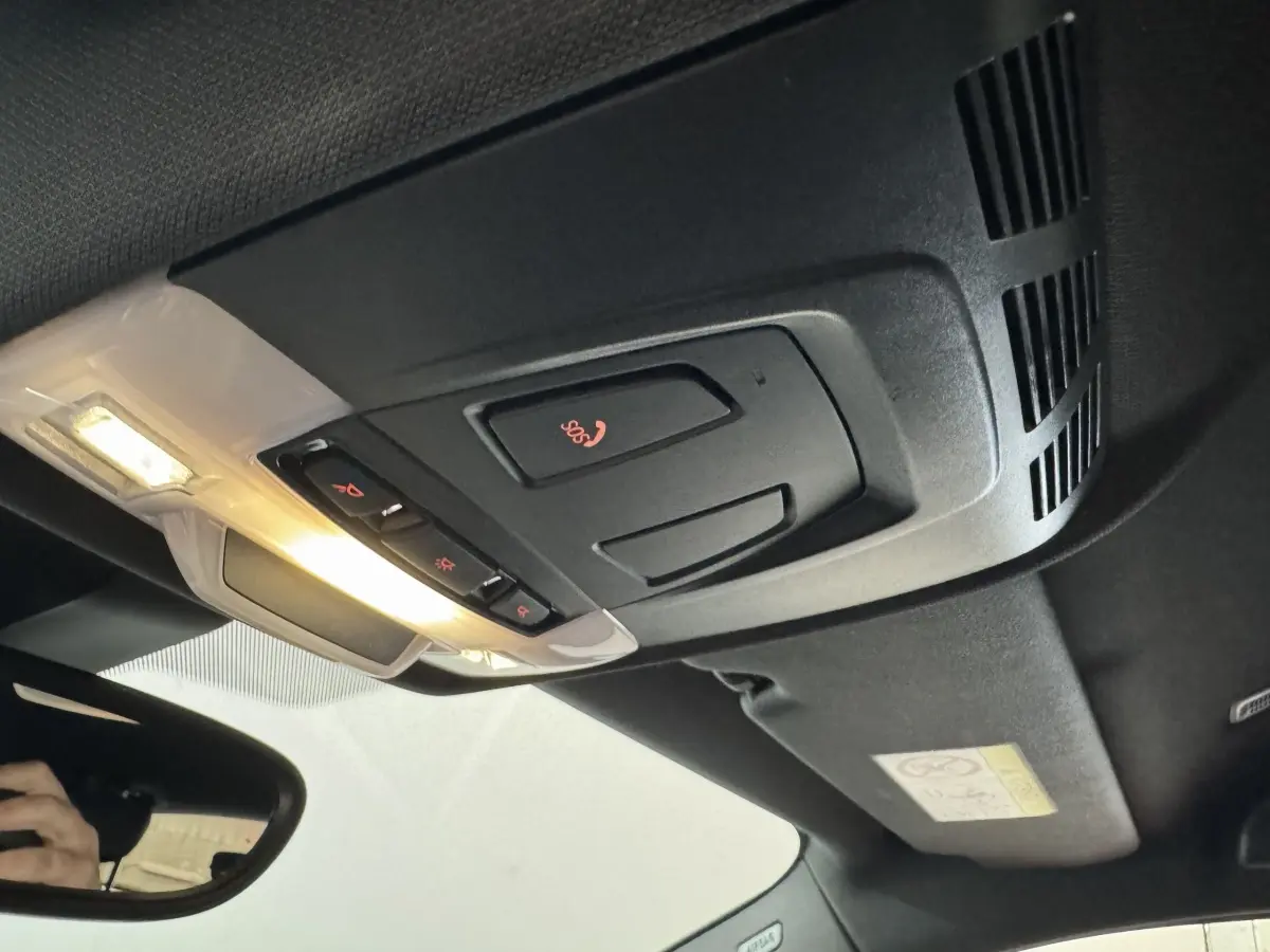 Vue intérieure en plongée du plafonnier noir avec commandes SOS et éclairage allumé d'une BMW X2 bleu hybride rechargeable.