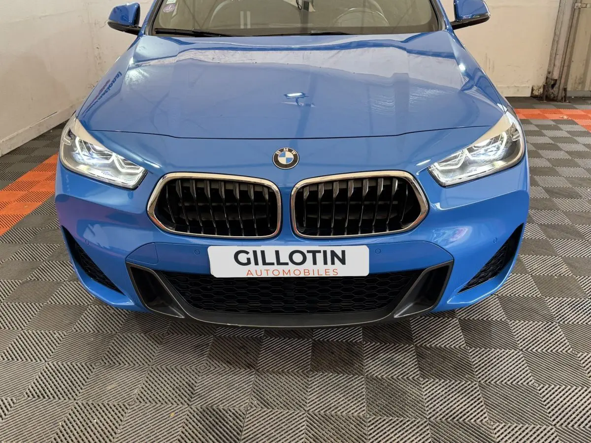 Vue frontale rapprochée d'une BMW X2 xDrive25e M Sport bleu avec calandre noire et phares allumés.