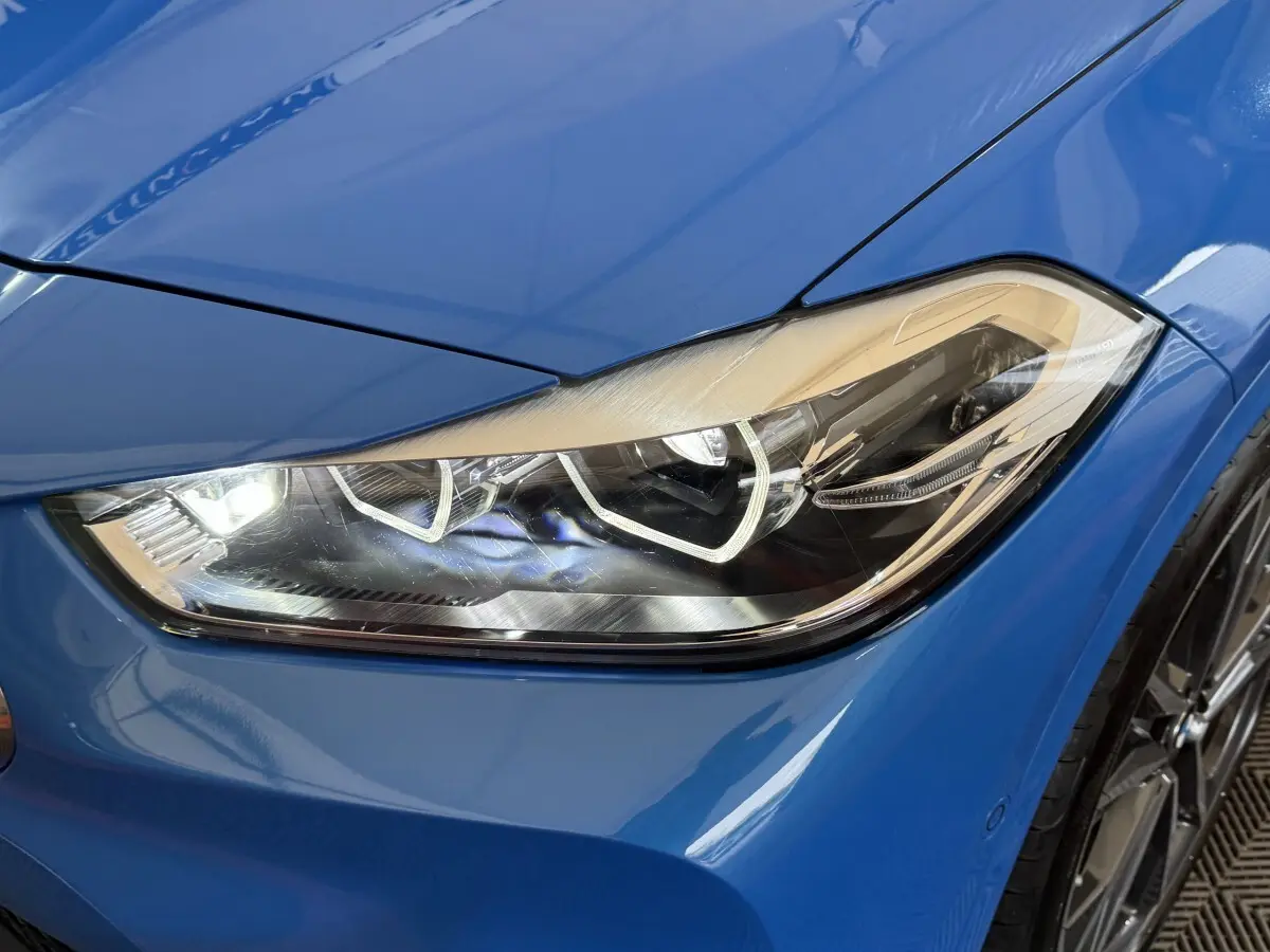 Gros plan sur le phare avant droit bleu vif d'une BMW X2 xDrive25e M Sport 2021, détails LED visibles.