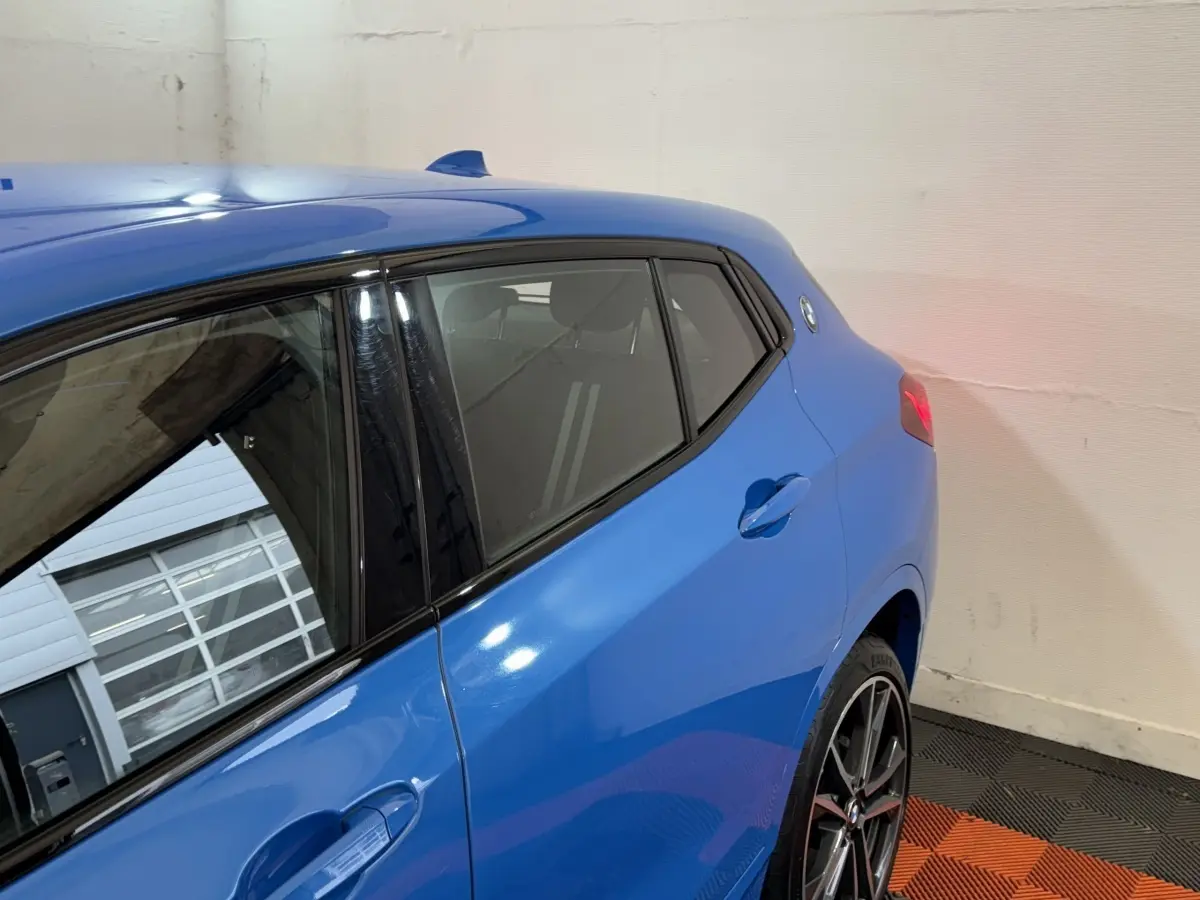 Vue 3/4 arrière côté gauche du BMW X2 xDrive25e M Sport bleu avec jantes sport et feux arrière allumés.