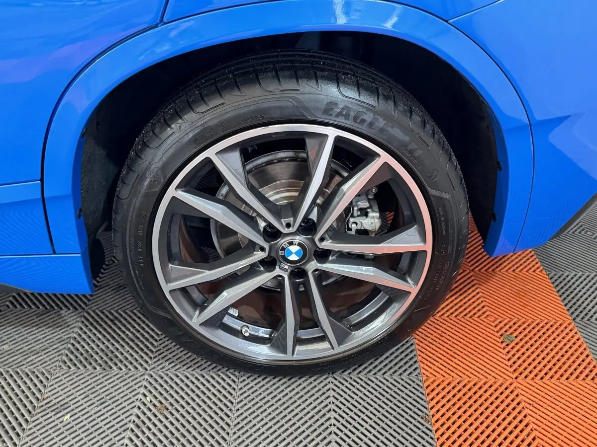 Gros plan sur la roue avant droite d’un BMW X2 bleu, avec jante alliage à branches doubles et logo BMW central.